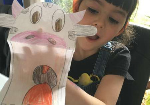 Ta sama dziewczynka pokazuje krowę z papieru z otwartą mordką (praca w 3D)